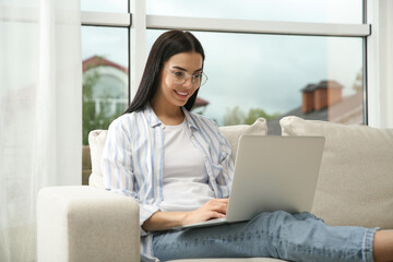 Fototapeta premium Young woman with laptop on sofa at home
