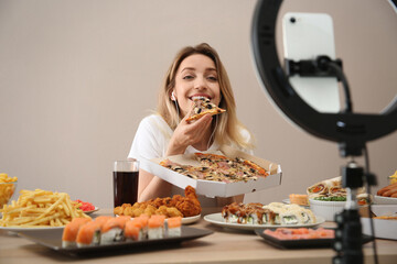 Food blogger recording eating show on smartphone camera against beige background. Mukbang vlog