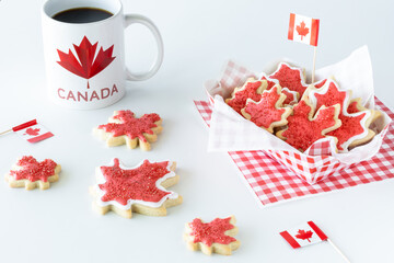 A checkered tray of Canada flag sugar cookies with a cup of coffee against a white background.