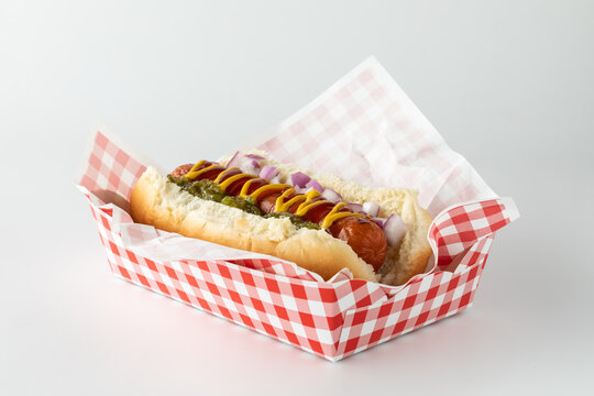 A frankfurter in a disposable checkered tray isolated against a white background.