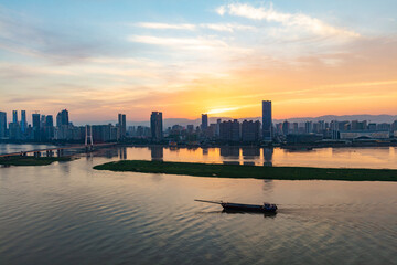 Nanchang, Jiangxi - June 8, 2021: In midsummer, the Ganjiang River is full of water, with ships passing by, tall buildings on both sides, and the city skyline is dazzled by the setting sun.