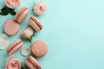 Obraz premium Flat lay composition with pink macarons and roses on light blue background. Space for text