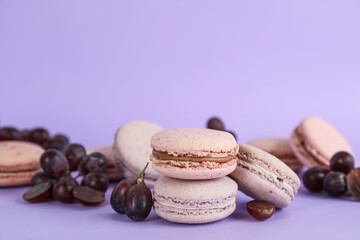Delicious macarons and grapes on violet background, space for text