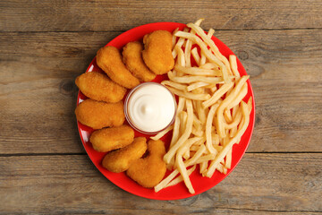 Tasty chicken nuggets and French fries served with mayonnaise on wooden table, top view