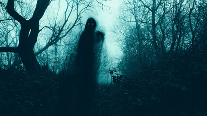A horror concept of a blurred scary hooded figure with glowing eyes on a path through a moody misty winter woodland