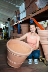 Young woman customer choosing big clay pot for garden in the store