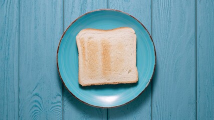 Piece of white toasted bread on a plate on a blue background. Top view.