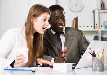 Young woman and man colleagues working at laptop and discussing in office