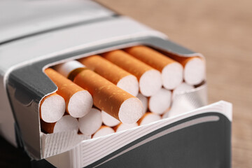 Cigarettes with orange filters in pack on table, closeup