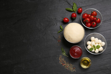 Raw pizza dough and other ingredients on black table, flat lay. Space for text