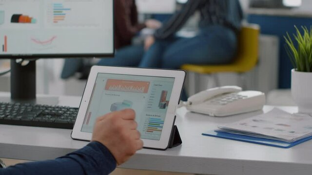 Paralysed business man sitting immobilized in wheelchair working at tablet and computer in same time analysing financial graphs, pc showing data prosessing on display for project regarding economy