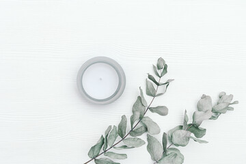 Scented candle in glass jar with natural ingredients on white wooden background with branches of eucalyptus