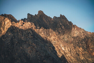 Scenic mountain landscape with great rocks in golden sunlight. Awesome rocky wall with sharp top in gold sunshine. Colorful sunny scenery with high rocky mountain with pointed pinnacle. Mountain wall.