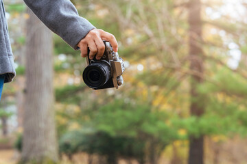 Fototapeta premium close up female traveller hand hold camera in one hand standing in autumn brown falling tree leaf public nature garden park travel concept