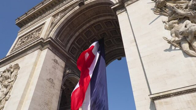 French flag flying in the wind under the Arc de Triomphe and facade bas reliefs, sculptures and engravings - Paris, France
