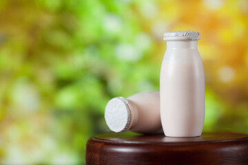 Natural liquid yogurt with probiotics in small plastic bottles on wooden table on background of green trees.