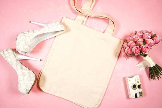 Wedding and bridal party theme canvas tote bag SVG craft product flat lay mockup styled stock photo. Styled with high heel bride shoes and bouquet on a textured pink background.