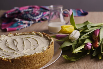 A cake, greeting flowers, a jug of milk, and a woman's silk scarf are laid out on a wooden table.