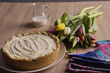 A cake, greeting flowers, a jug of milk, and a woman's silk scarf are laid out on a wooden table.