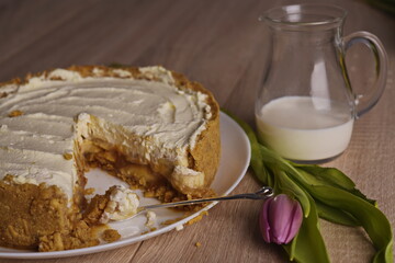 A piece of cake, a jug of milk, and a tulip are spread out on the table.