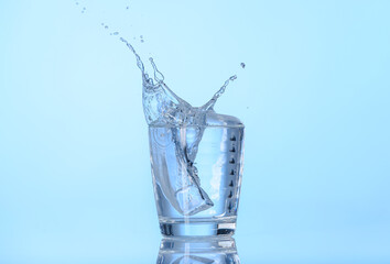 Glass of water with splash on color background