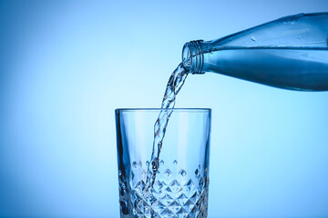 Pouring water from bottle into glass on color background