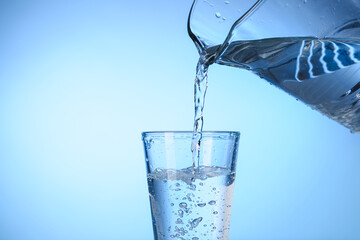 Pouring water from jug into glass on color background