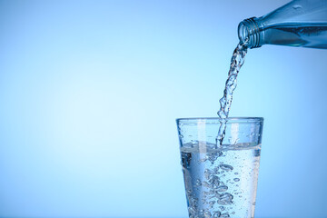 Pouring water from bottle into glass on color background