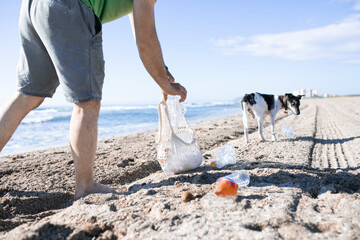 Man and his dog cleaning the beach of plastic bottles