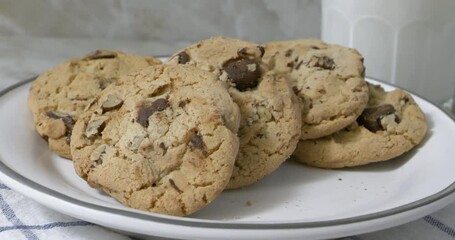 Closeup of a hand taking a chocolate chip cookie from a plate of cookies