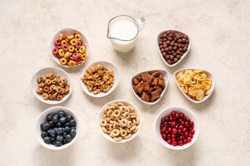 Bowls with different cereals, berries and milk on light background