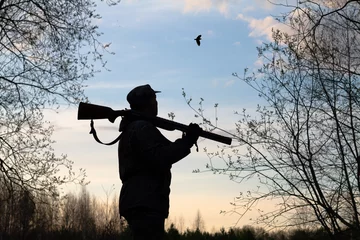Foto op Canvas a hunter with a rifle on his shoulder looks at a flying woodcock late at night © rodimovpavel