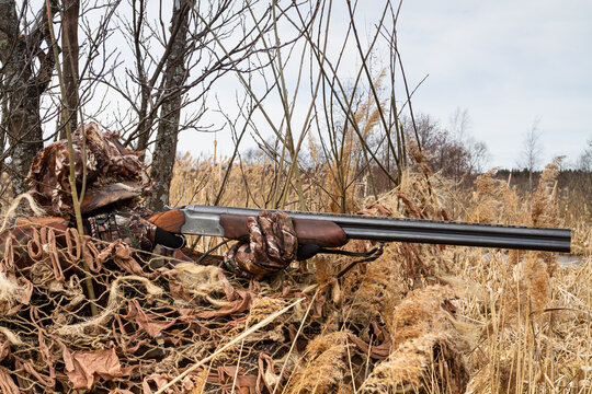 a duck hunter sits in a camouflaged hideout and aims a shotgun