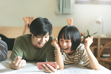 Young adult asian lover couple using mobile phone cheer up for watch sports streaming at bedroom.