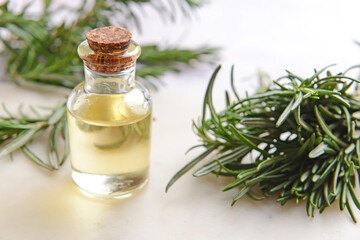 Bottle of essential oil and fresh rosemary on light background, closeup