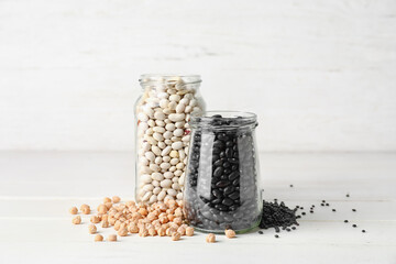 Jars with raw beans and different legumes on light background