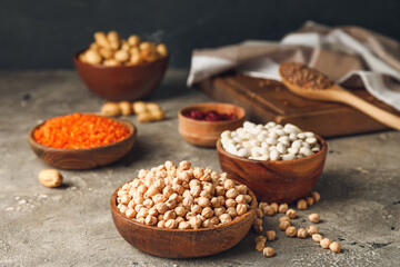 Bowls with different legumes on grey background