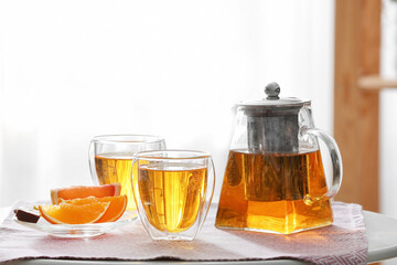 Teapot and cups of hot beverage on table in room