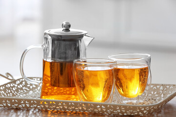 Teapot and cups of hot beverage on table in room