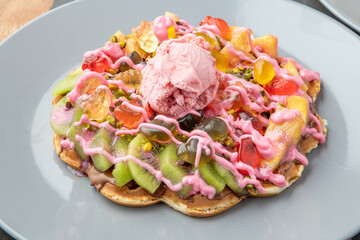 Heart waffle with kiwi and pineapple with gummy candy and ice cream on it.