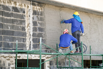 Fototapeta premium Plasterers using and operating sprayer mortar equipment machine for spraying mortar concrete cover brick wall and plastering for the decoration finishing work at the construction site