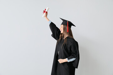 Happy female graduating student with diploma on light background