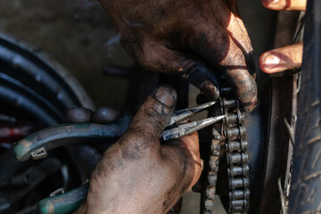 A middle aged man practicing a car in a car shop in Thailand is replacing a motorcycle chain.