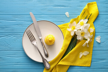 Beautiful table setting with narcissus flowers and cupcake on color wooden background