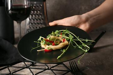 Woman holding plate with tasty pasta and fresh sprouts on dark background, closeup