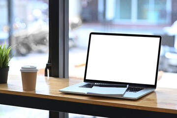 Mock up laptop, notebook and coffee cup on wooden table near window.