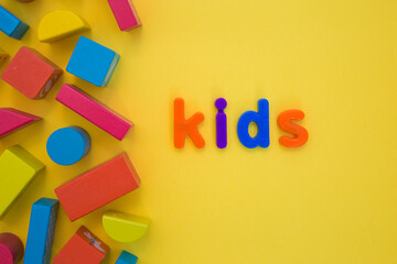Kids Education, Creative, logical thinking concept. Colourful multicoloured building wooden toy blocks for children learning development word Kid from plastic letters on yellow background flat lay