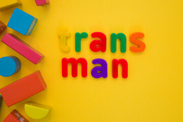 Transgender or cisgender LGBTQ plus pride concept. Different colourful plastic letters make the word Trans boy kid on the bright yellow background. Defining yourself, be proud of who you are