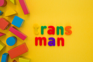 Transgender or cisgender LGBTQ plus pride concept. Different colourful plastic letters make the word Trans boy kid on the bright yellow background. Defining yourself, be proud of who you are