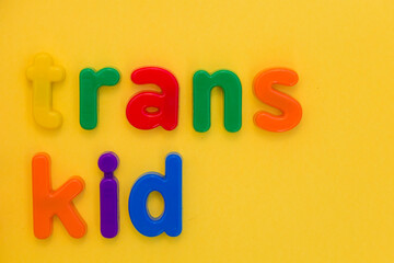 Transgender or cisgender LGBTQ plus pride concept. Different colourful plastic letters make the word Trans boy kid on the bright yellow background. Defining yourself, be proud of who you are